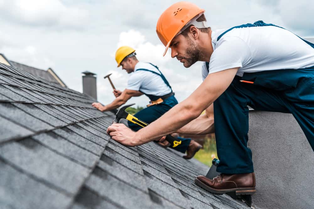 two roofers on a roof repairing it